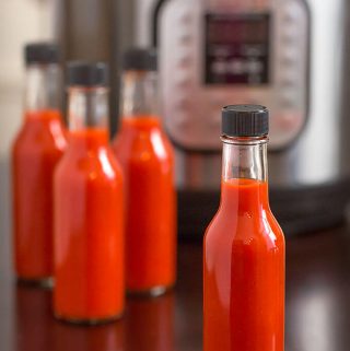 Four bottles of red hot sauce in front of pressure cooker