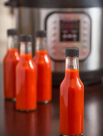 Four bottles of red hot sauce in front of pressure cooker