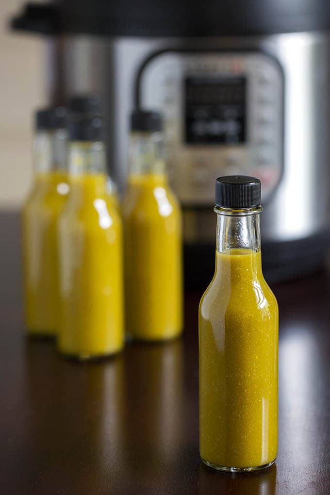 Several bottles of green hot sauce in front of pressure cooker