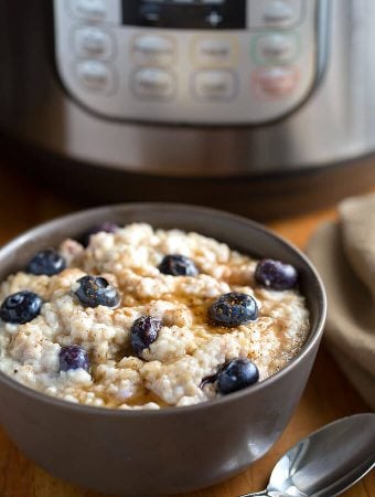 Steel Cut Oats in a dark grey bowl topped with blueberries with a pressure cooker in the background