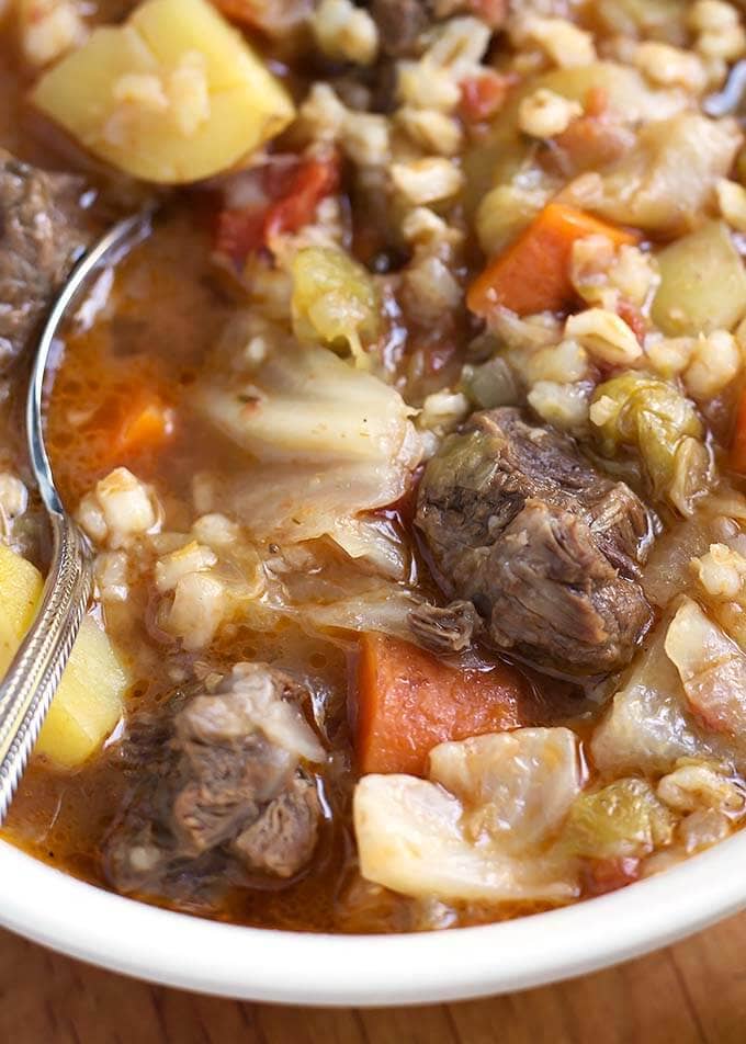 Close up of Beef Barley Vegetable Soup in white bowl with spoon
