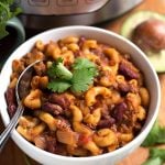 Chili Mac in a white bowl with spoon on wooden board