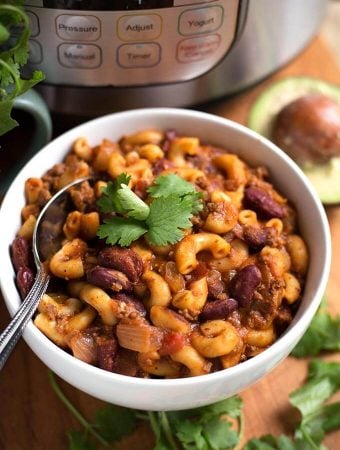 Chili Mac in a white bowl with spoon on wooden board