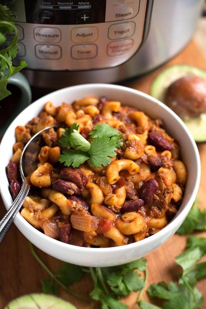 Chili Mac in a white bowl with spoon on wooden board