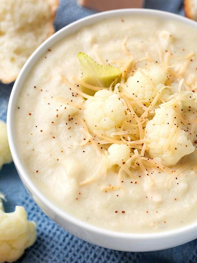 Close up of Smoky Creamy Cauliflower Soup in a white bowl next to bread and cauliflower florets 