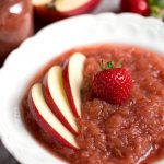 Strawberry apple sauce in a white bowl topped with sliced apples and a strawberry