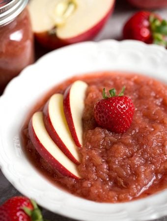 Strawberry apple sauce in a white bowl topped with sliced apples and a strawberry