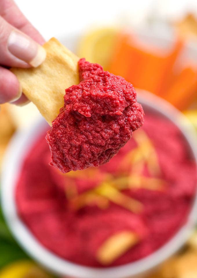 Close up of Red Beet Hummus on a pita chip held by human fingers