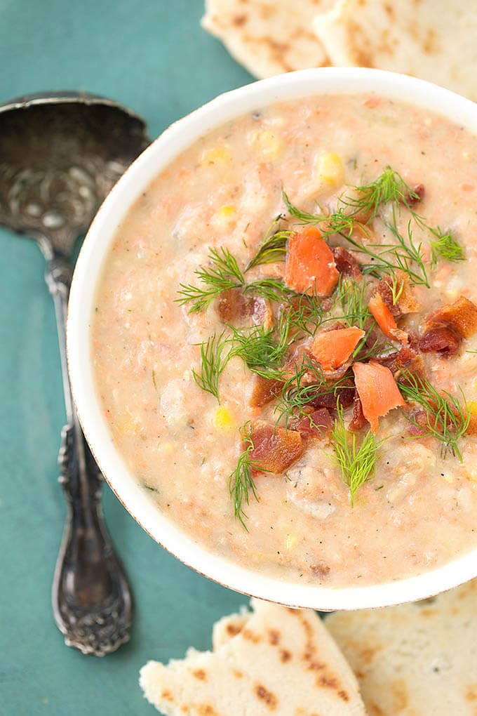 Salmon Chowder garnished with dill in a small white bowl on a turquoise plate with a silver spoon and torn flat bread