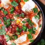 Shakshouka - Eggs in Purgatory in a black bowl next to a wooden spoon