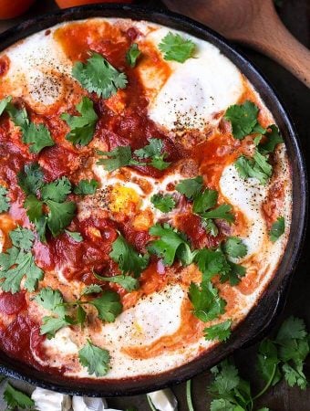 Shakshouka - Eggs in Purgatory in a black bowl next to a wooden spoon