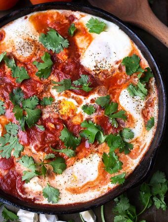 Shakshouka - Eggs in Purgatory in a black bowl next to a wooden spoon