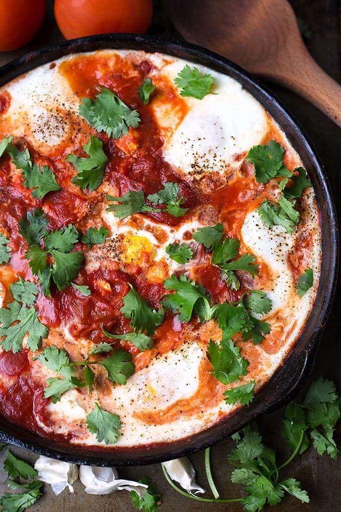 Shakshouka - Eggs in Purgatory in a black bowl next to a wooden spoon