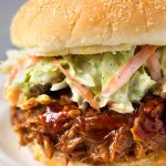 Slow Cooker BBQ Pulled Pork with coleslaw on hamburger bun on white plate