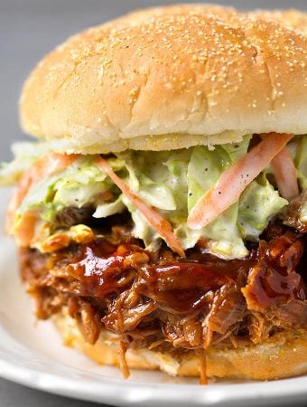 Slow Cooker BBQ Pulled Pork with coleslaw on hamburger bun on white plate