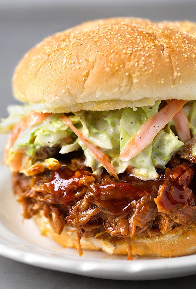  Slow Cooker BBQ Pulled Pork with coleslaw on hamburger bun on white plate