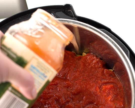 Liquid poured out of glass jar into pressure cooker pot with other ingredients