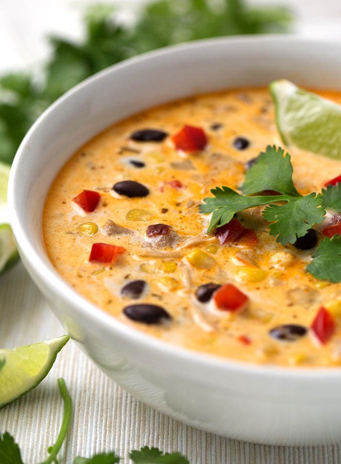 Close up of Crock Pot Mexican Corn Chicken Soup in white bowl garnished with cilantro leaves and lime wedges