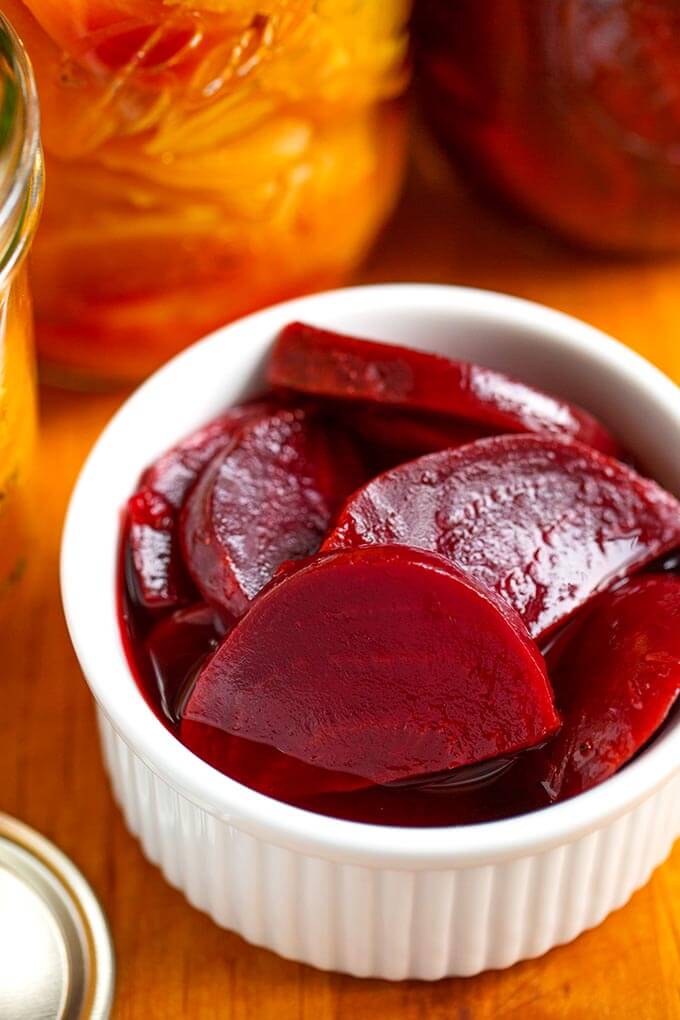 Close up of pickled beets in small glass bowl on wooden board