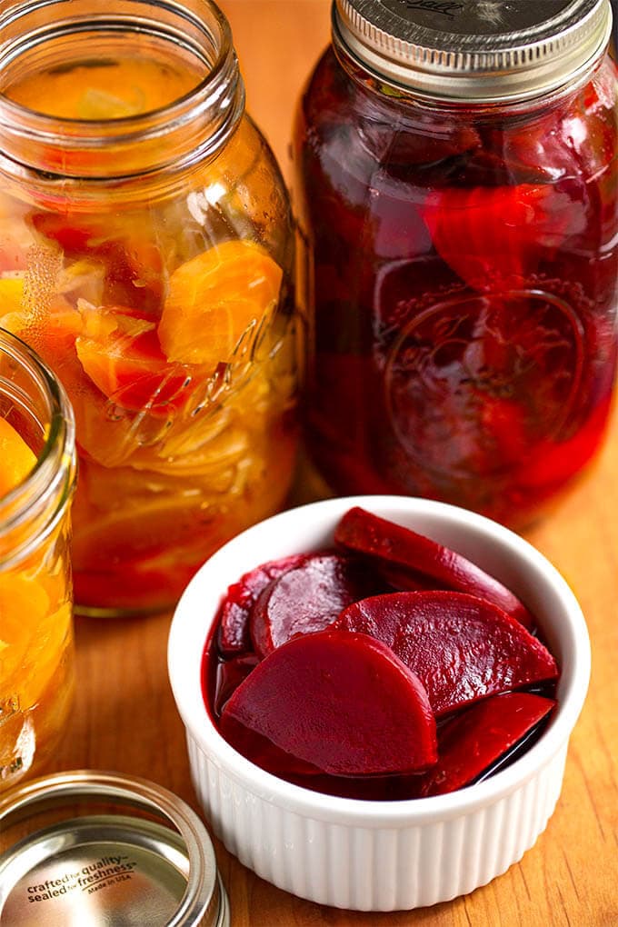 Pickled Beets in a small white bowl with canning jars in the back ground on wooden board