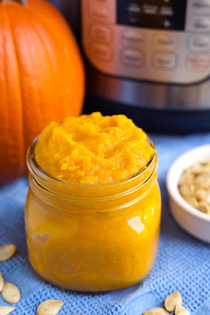 small glass canning jar of pumpkin puree with pumpkin and pressure cooker in background