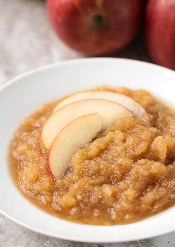 Applesauce in a shallow white bowl with sliced apples with pressure cooker and apples in background