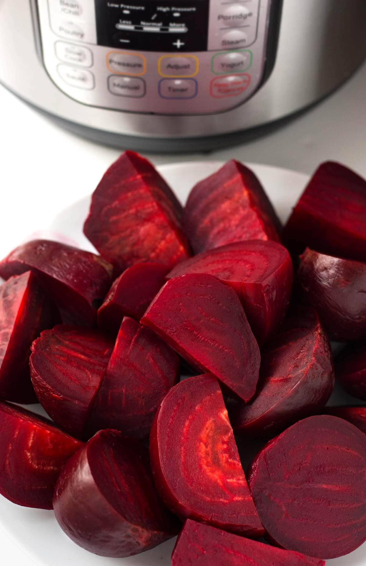 Cooked quartered instant pot beets on white plate with pressure cooker in the background.