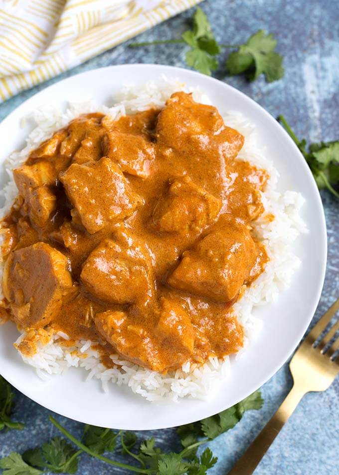 Butter Chicken over rice on white plate next to gold fork