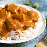 Butter Chicken over rice on white plate next to gold fork