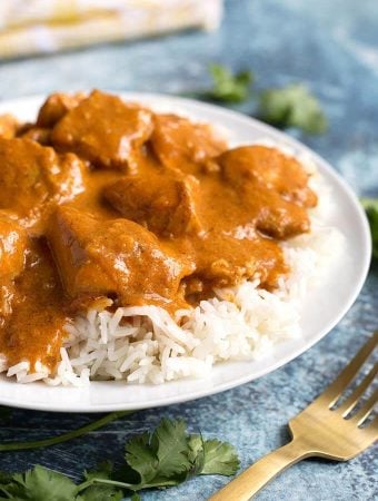 Butter Chicken over rice on white plate next to gold fork