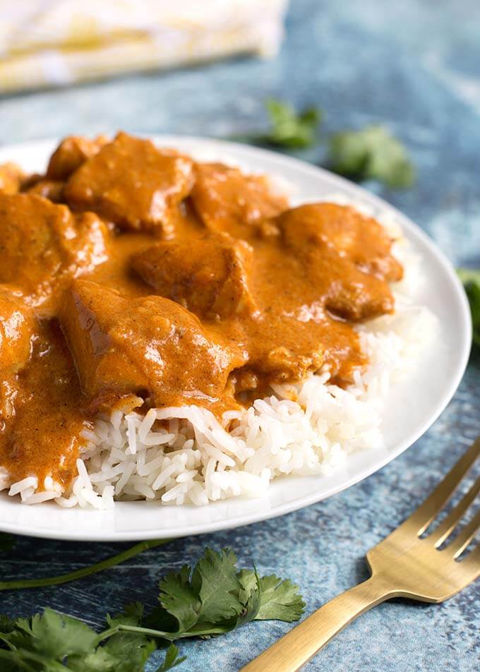 Butter Chicken over rice on white plate next to gold fork