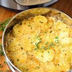 Cheesy Scalloped Potatoes in a round pan on a wooden board with pressure cooker in background