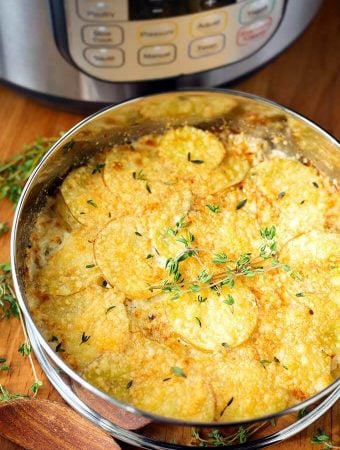 Cheesy Scalloped Potatoes in a round pan on a wooden board with pressure cooker in background
