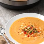 Fresh Corn Soup in a shallow white bowl next to silver spoon and pressure cooker