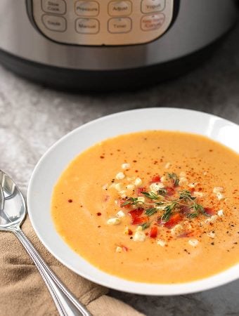 Fresh Corn Soup in a shallow white bowl next to silver spoon and pressure cooker