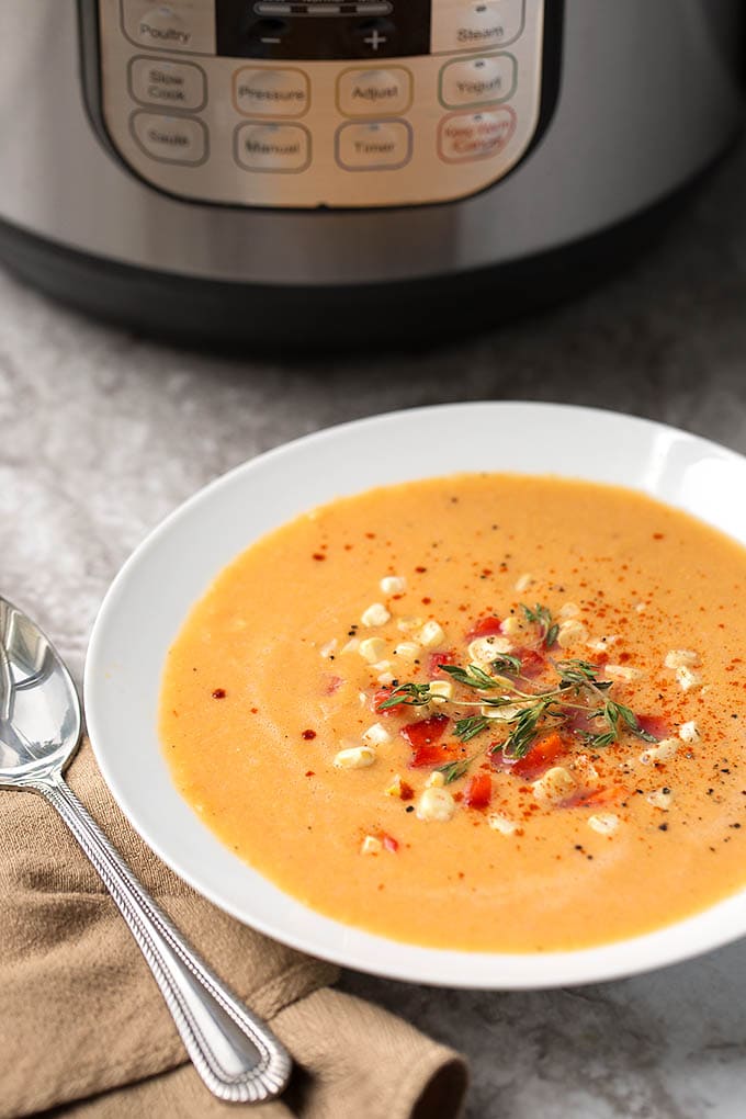 Fresh Corn Soup in a shallow white bowl next to silver spoon and pressure cooker