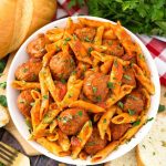 Meatball Pasta Dinner in a white bowl on wooden board next to golden fork and slices of bread