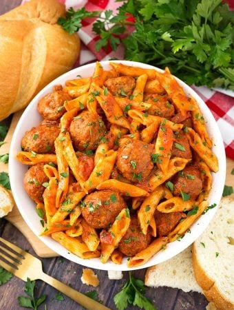 Meatball Pasta Dinner in a white bowl on wooden board next to golden fork and slices of bread