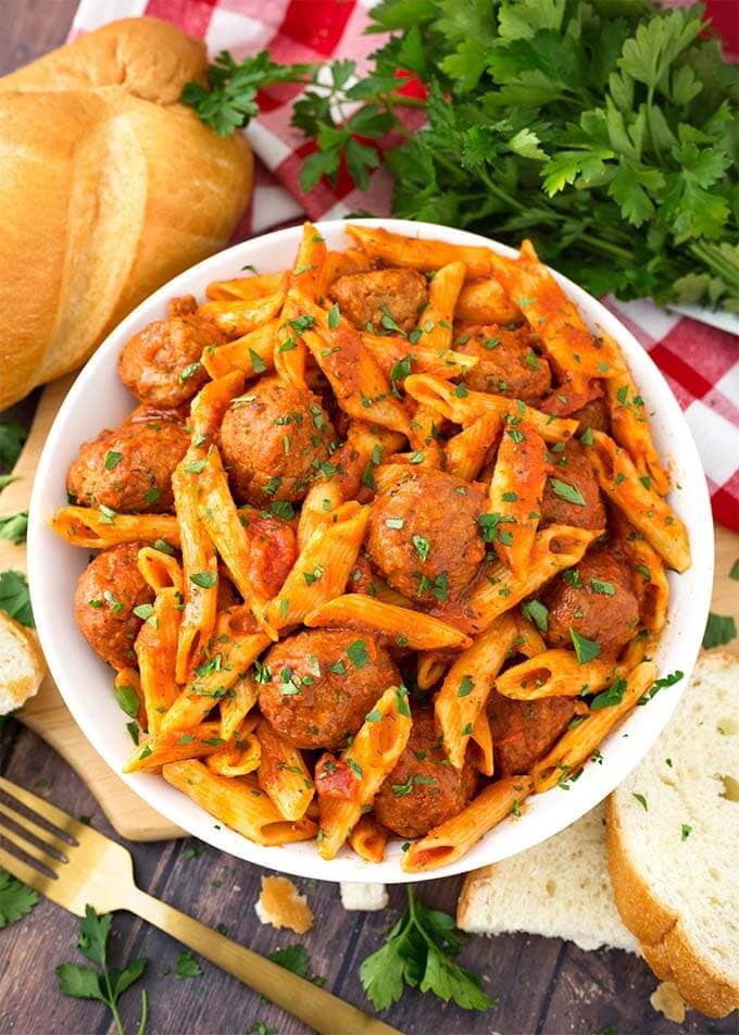 Meatball Pasta Dinner in a white bowl on wooden board next to golden fork and slices of bread