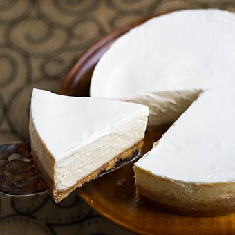 Slice of New York Cheesecake on brown plate lifted from rest of cake by serving spoon 