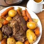 Pot Roast on a white plate next to a small pitcher of gravy and pressure cooker