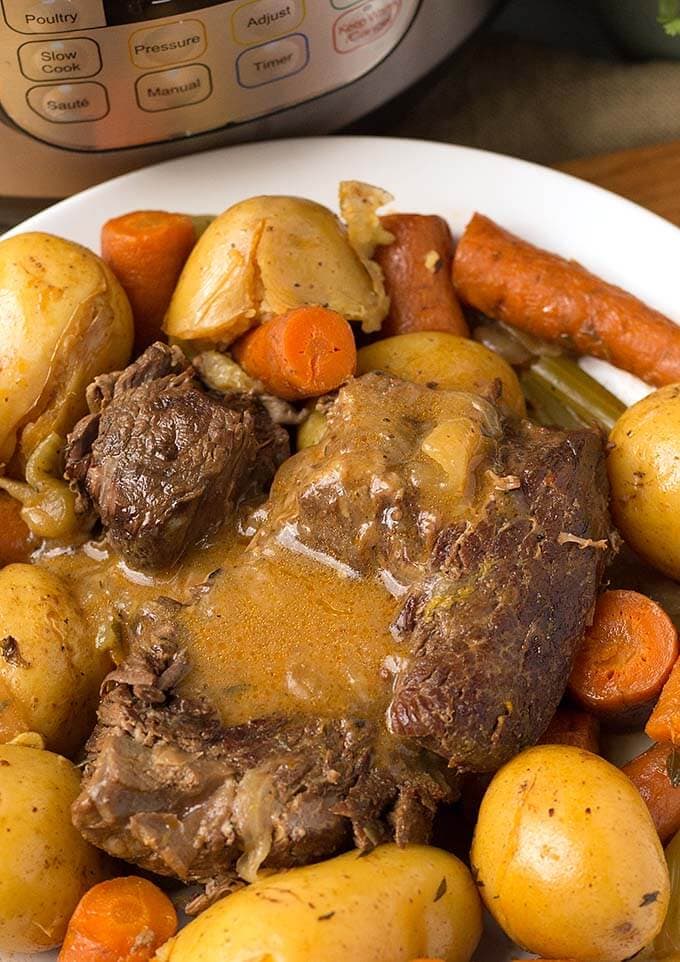  Pot Roast with potatoes and carrots on a white plate next to pressure cooker