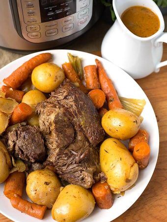 Pot Roast on a white plate next to a small pitcher of gravy and pressure cooker