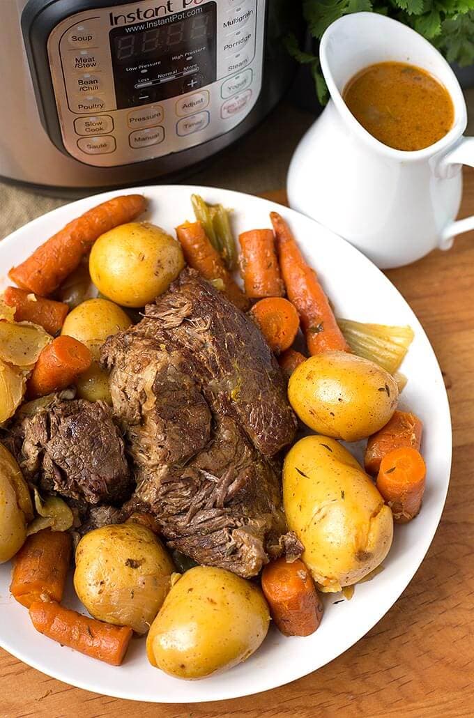 Instant Pot Simple Pot Roast on a white plate with gravy pitcher and pressure cooker in background