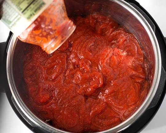 Jar of pasta sauce poured into pressure cooker pot