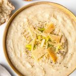 Smoky Creamy Cauliflower Soup in a light brown bowl on white background with crusty bread and spoon