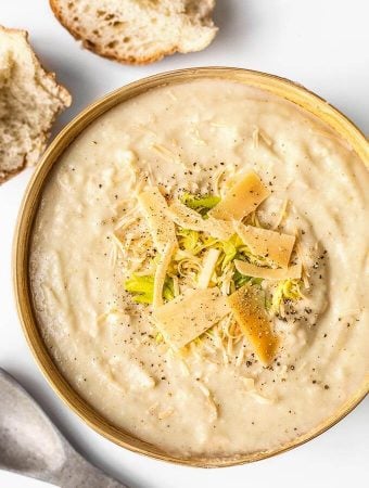 Smoky Creamy Cauliflower Soup in a light brown bowl on white background with crusty bread and spoon
