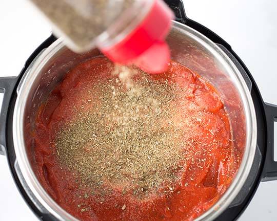 Seasonings being poured over pasta sauce in pressure cooker pot