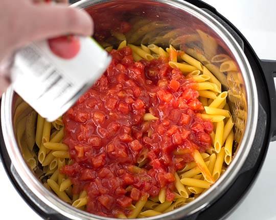 Diced tomatoes on top of dried pasta in pressure cooker pot