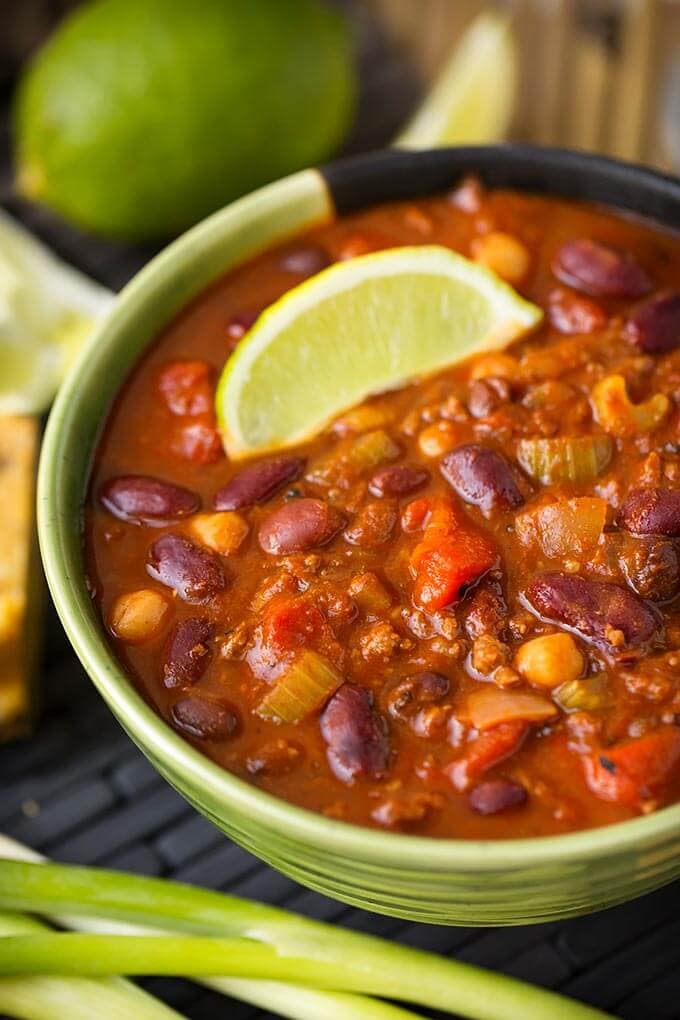 Chili in a green bowl next to green onion and limes